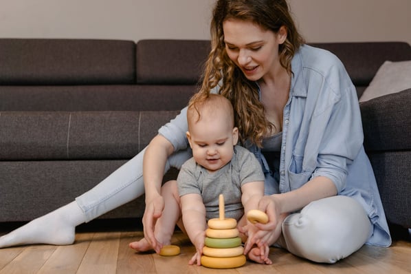A woman helps a toddler stack wooden rings on a pole. 