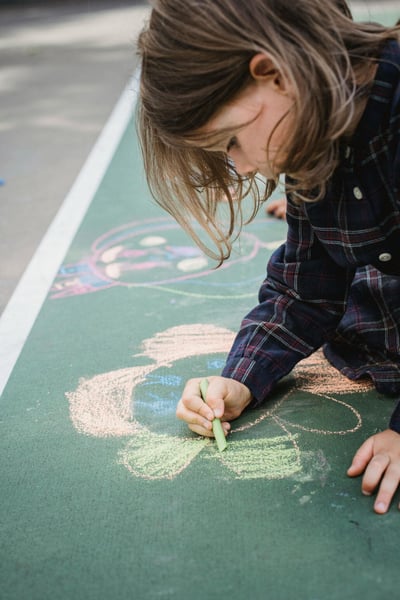 A child drawing a colorful flower on the ground with chalk.