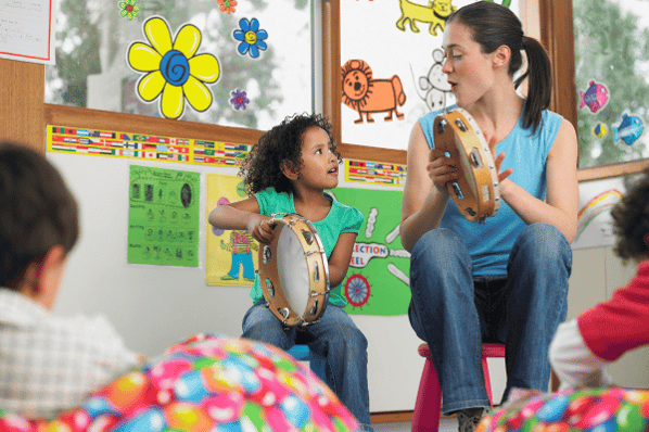 Careers in child development: Preschool teacher in music class shaking a tambourine with young girl