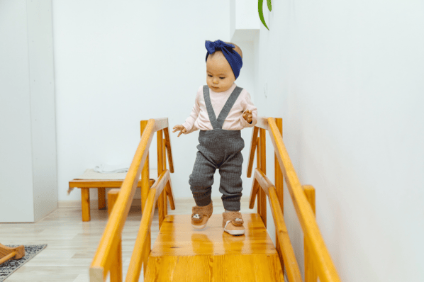 Toddler walking on top of a wooden slide.