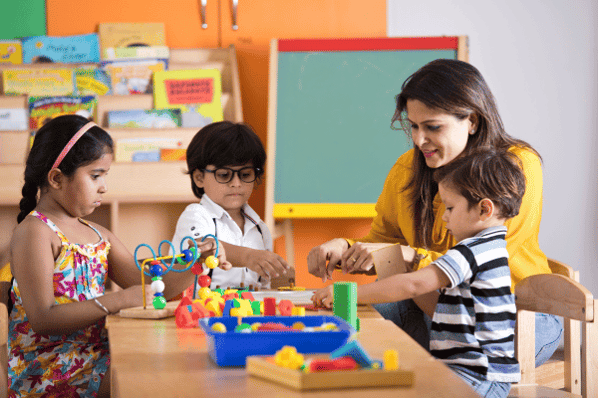Practicing preschool teacher skills by sitting at table with 3 preschool aged children as they play with blocks