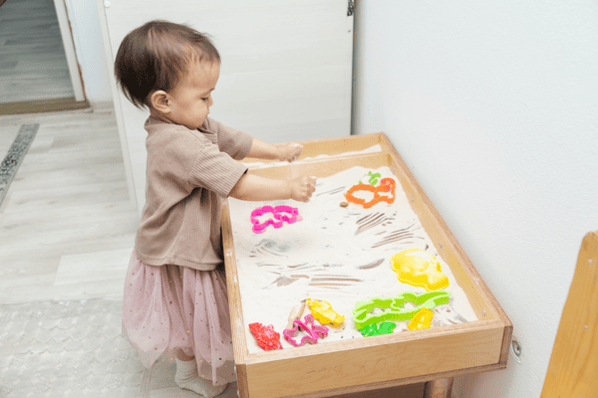Toddler playing with kinetic sand and plastic shapes.