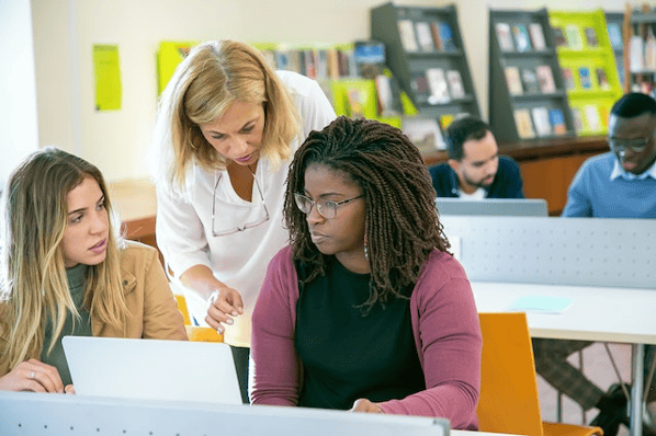 Two women sit at a computer while a third woman stands over their shoulders
