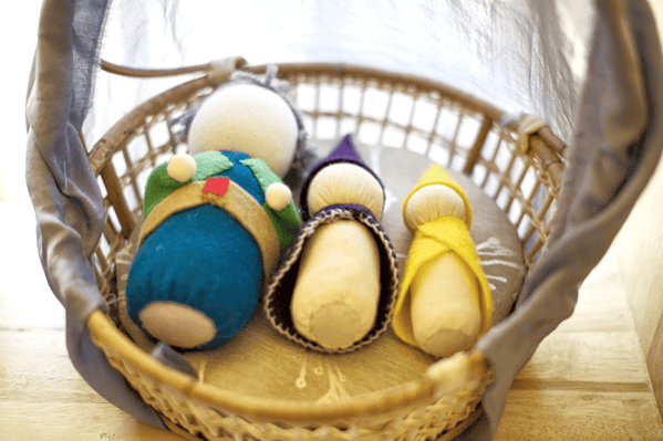 Three small Waldorf cloth dolls with no facial features in a basket.